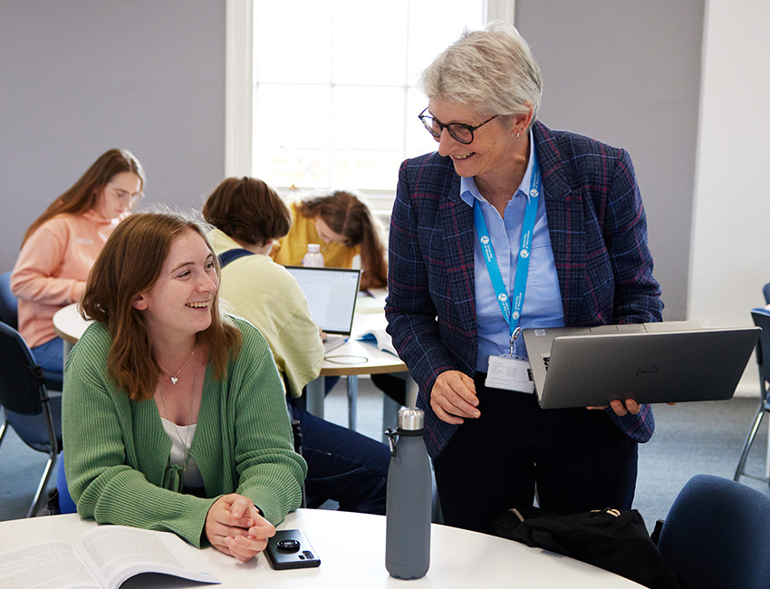 A lecturer support a student, laptop in hand