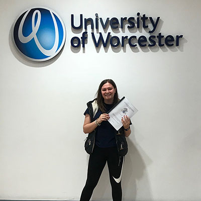 Young woman underneath the university of worcester sign and logo