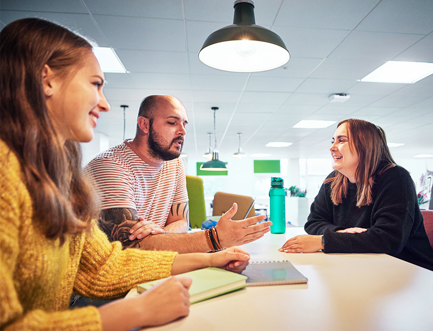 A small group of students discussing their work sat around a table with notebooks. 