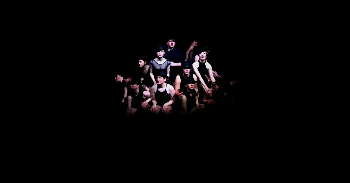A group of performers spot lit on a dark stage