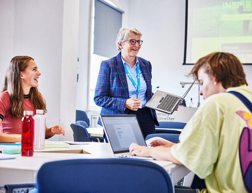 Students at a table with their laptops listening to their lecturer