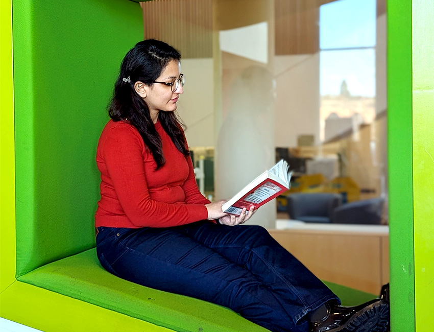Student sat in a comfy seat in the library reading a book