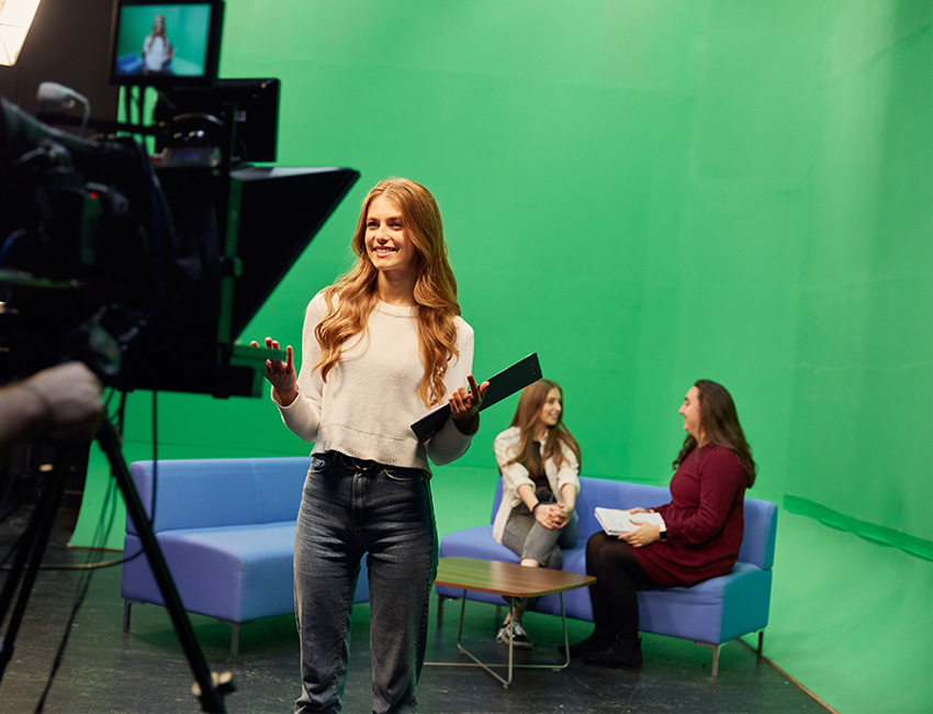 Student stood in front of a camera with a green screen in the background
