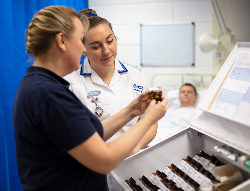 A nursing lecturer and nursing student looking at a small bottle of medicine in a mock hospital ward