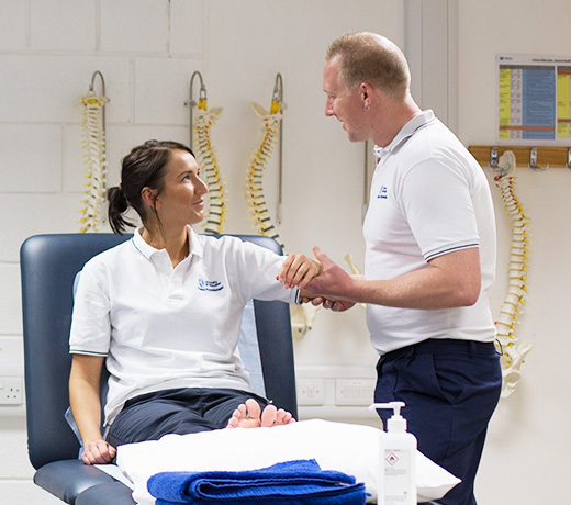 Instructor demonstrating an arm assessment on a student seated on a treatment table