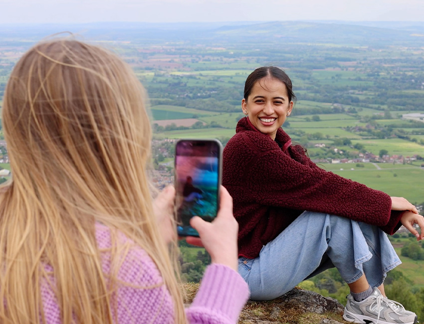 Student posing for a photo on top of the Malvern Hills, with a beautiful view of green countryside behind her
