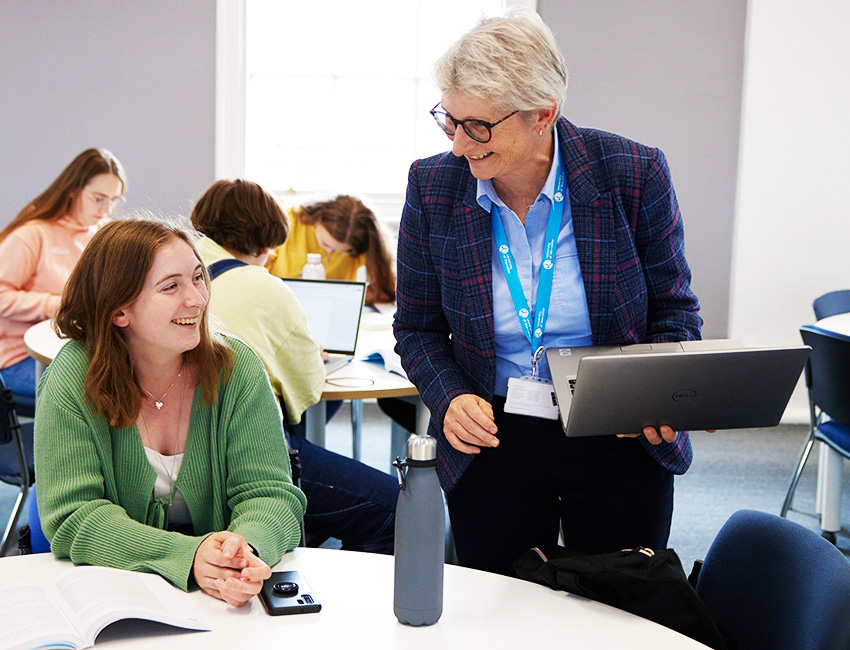 Student at a table ina  classroom laughing with their lecturer