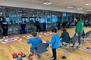 Children playing indoor curling while seated in Chairs with adult instructors