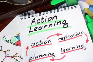 Action Learning underlined in green written on a note pad with Action, Reflection, Learning and Planning with red arrows linking them together