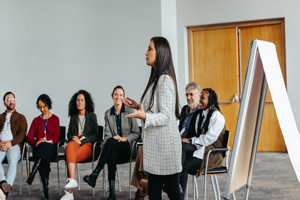 Woman standing in front of seated participants giving a presentation from a flipchart.