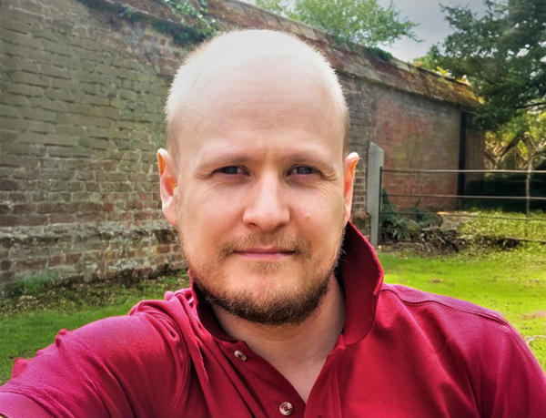 A man in a purple polo top, with nature in the background