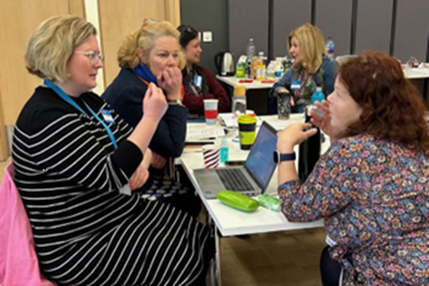 Five people around a table engaged in Storytelling In Action discussion.