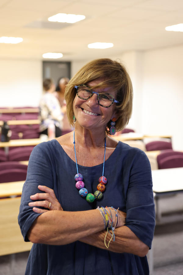 Sheena Byrom smiles to the camera in a blue jumper with a colourful necklace