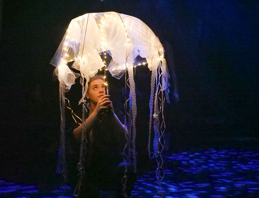 A girl mid performance, standing under an umbrella covered in lights