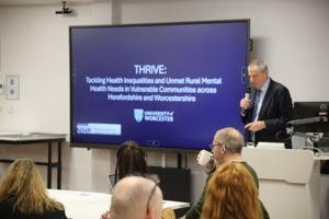 Professor David Green addresses the room holding a microphone