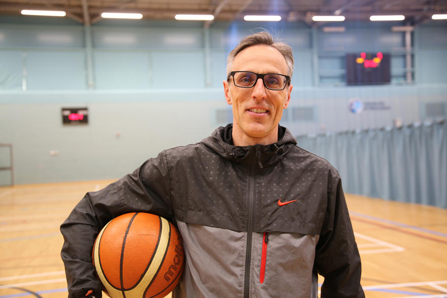 Alejandro Vaquera poses in an arena with a basketball under his arm, smiling for the camera