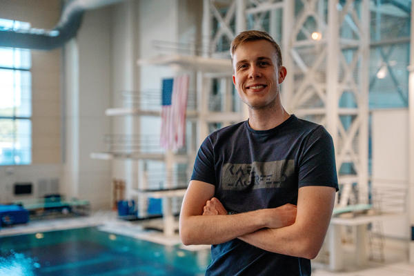 A man poses with arms folded in front of a swimming pool wearing a blue shirt