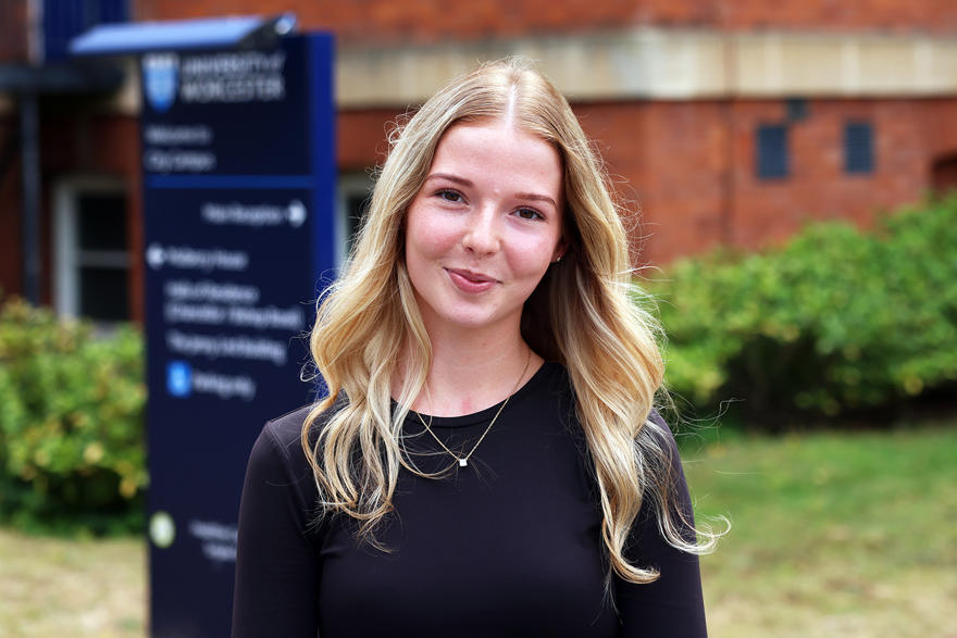 Student Beth Lammas  in front of a sign and a red brick venue