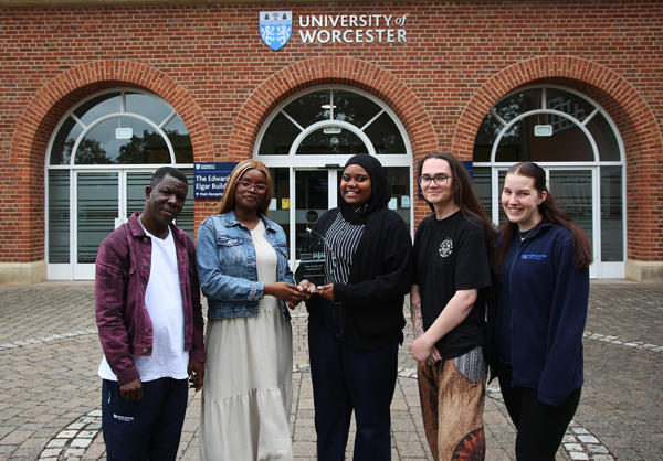 5 student officers pose outside the University of Worcester holding a glass award