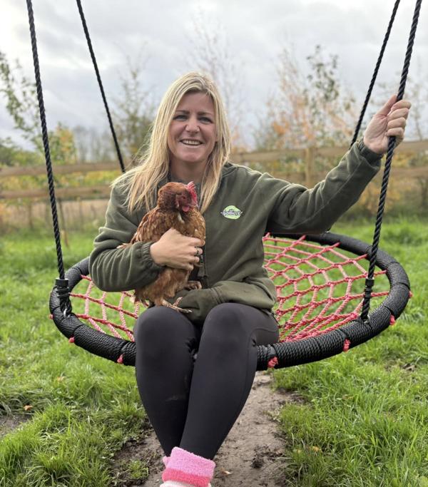 Emma Nokes smiles for the camera on a large swing while holding a chicken.