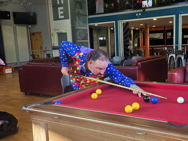 A man in a blue spotty shirt plays pool on a red table