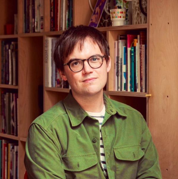 James Bailey in a green shirt, smiling for the camera in front of a bookcase