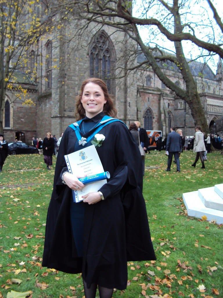 A graduate poses with their certificate outside Worcester Cathedral