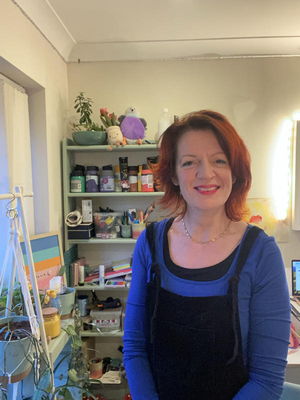 Lecturer Kaytie Holdstock stands in her art studio, smiling at the camera