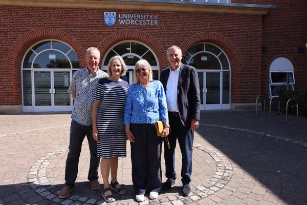Four people pose together in a row outside the University of Worcester main entrance