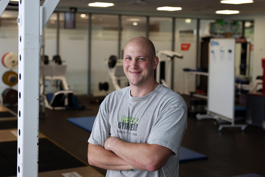 Matt Davies poses in a gym in a grey t shirt