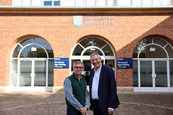 Two people pose outside the front doors of the university of worcester