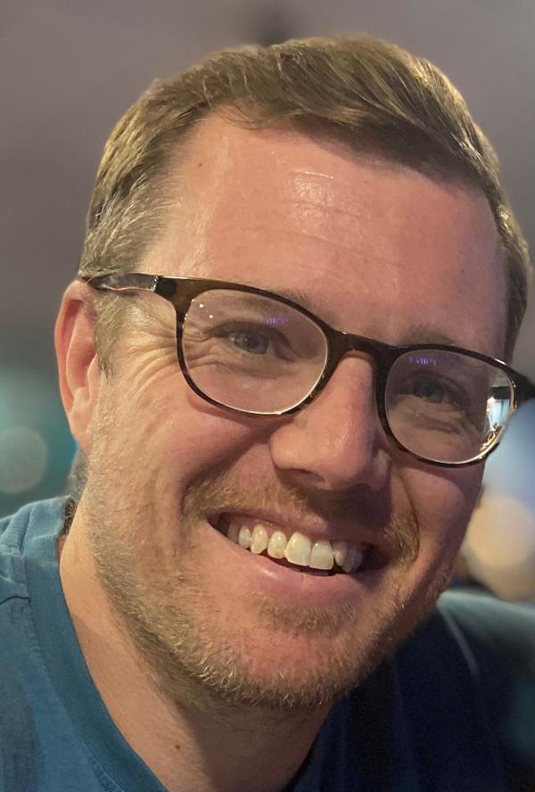 Mike Tyler smiles in a head and shoulders shot while wearing a blue top