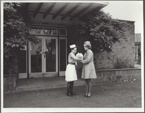 A black and white image of a mother being handed her baby by a midwife