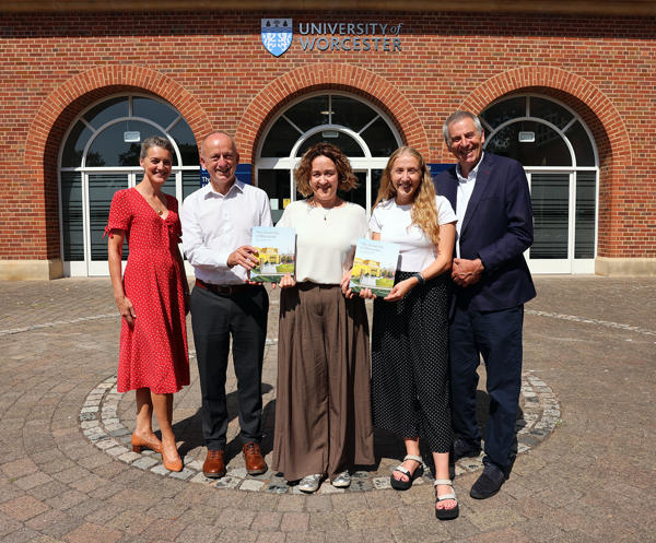 Five people pose holding books outside a red brick building
