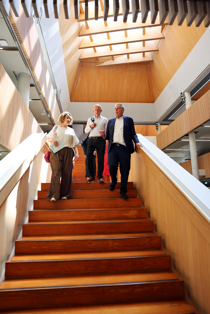 Three people walking down a wooden staircase in a grand open building