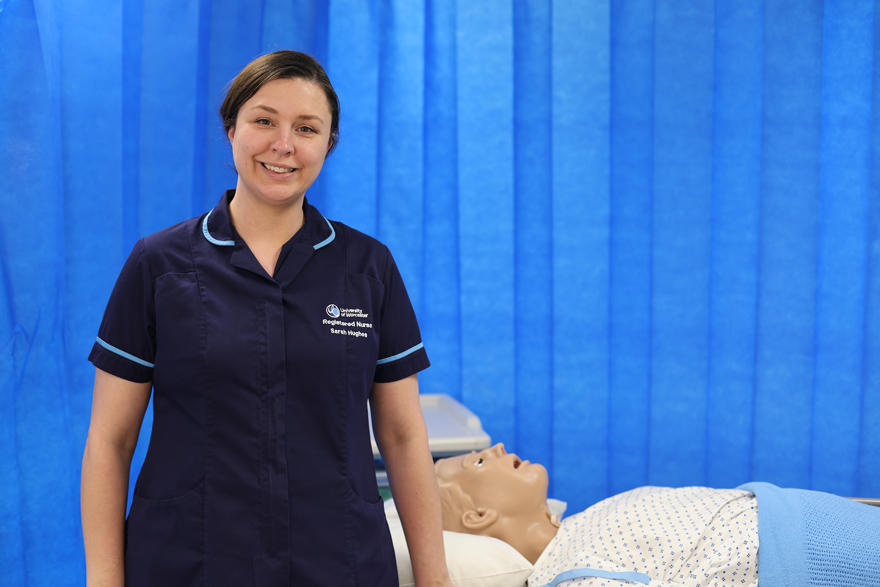 Sarah Hughes poses in a clinical setting in a nurses uniform next to a medical dummy