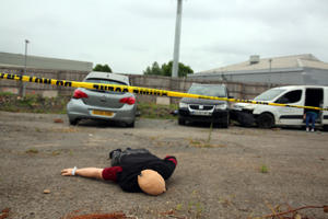 A dummy lays on the ground near the crash scene
