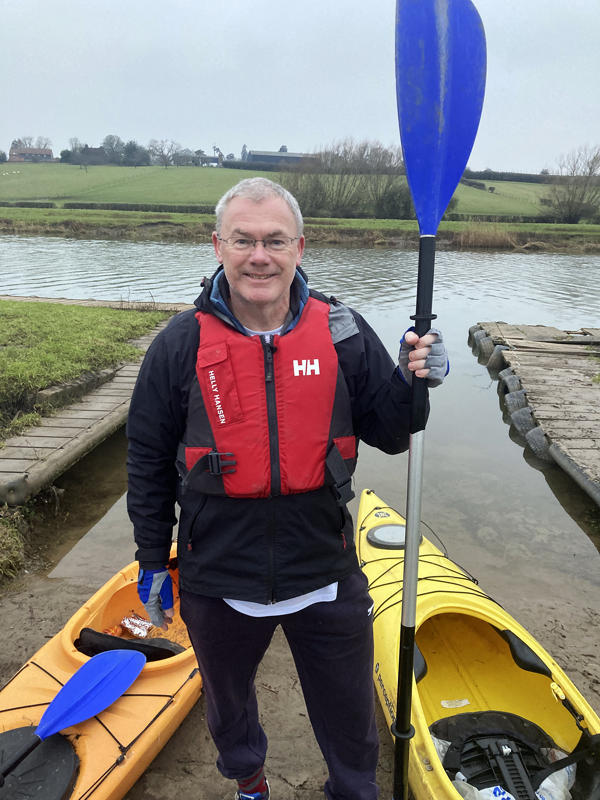 Steve poses with his paddle next to his yellow canoe with a lifejacket on