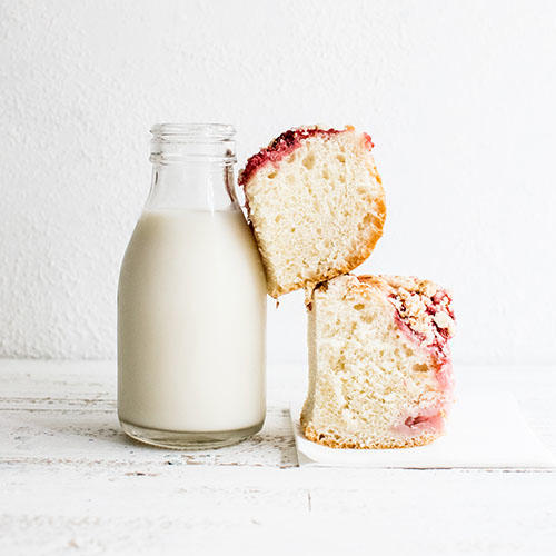 2 square pieces of cake are balanced against a small glass bottle of milk.