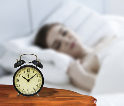 A woman asleep in a bed with a clock next to her on a bedside table