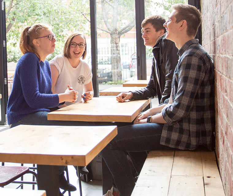 Two female and two male students casually dressed and sat chatting and laughing around a table in a quiet restaurant.