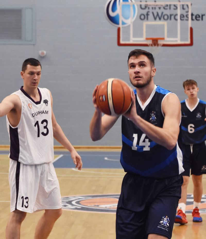 Three basketball players, one is holding a basketball preparing to throw