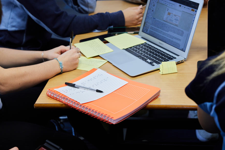 Student making study notes at a desk with their notebook ans laptop
