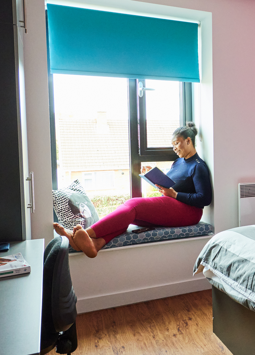 Student reading on window sill in bedroom