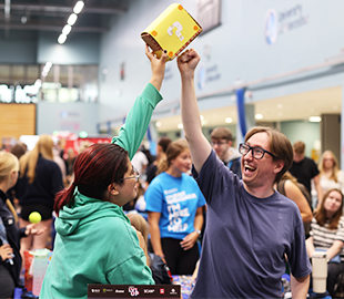 Two students from gaming society reach to tap a golden brick