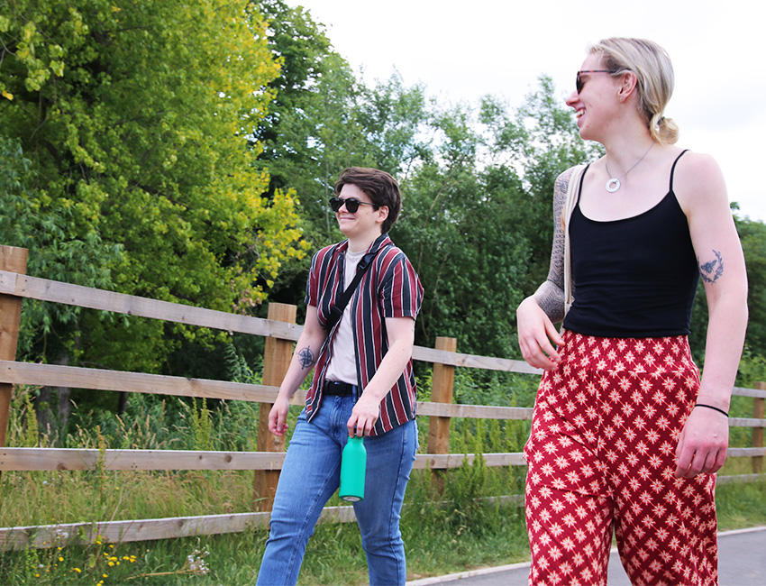 Two students chatting on a walk with grass and trees beside them