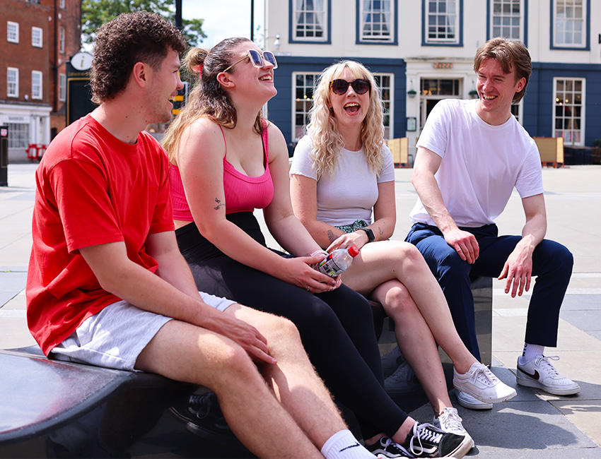 Four students sat laughing together in summer clothing with the city in the background