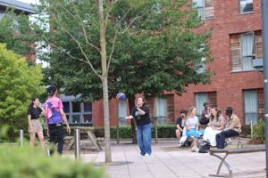 Students playing catch and sitting on picnic benches outside their accommodation on campus