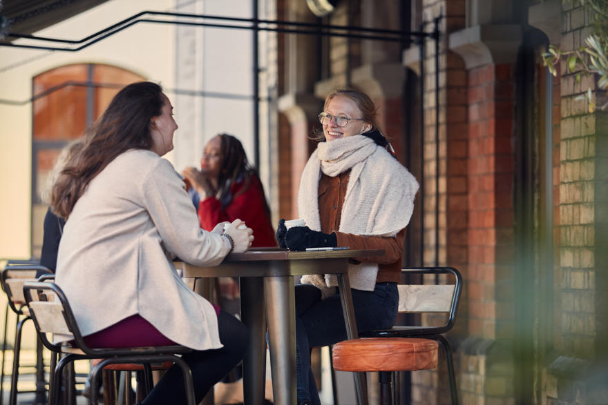 Two students dressed warmly sat outside a cafe