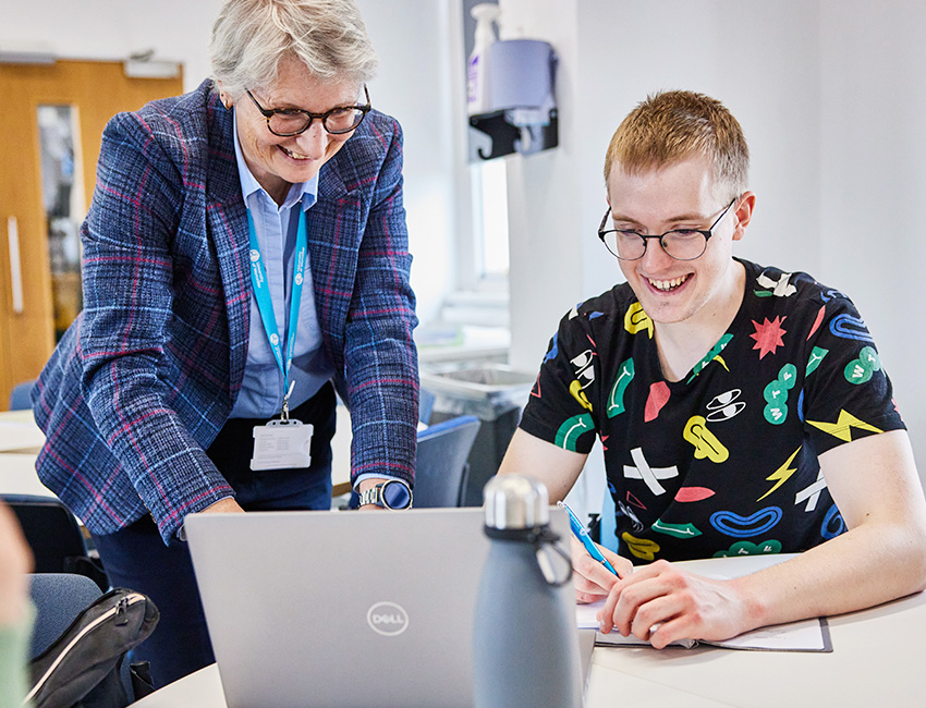 A business lecturer helping a student with a laptop
